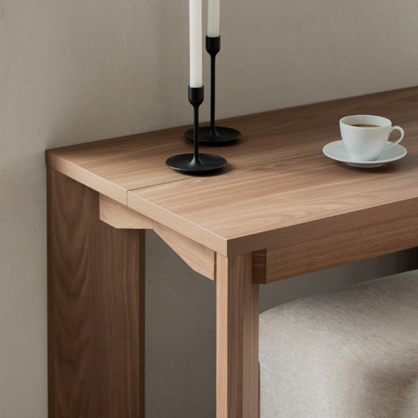 Close up lifestyle image of walnut wood extendable dining chair collapsed showing it in the smallest size against the wall.