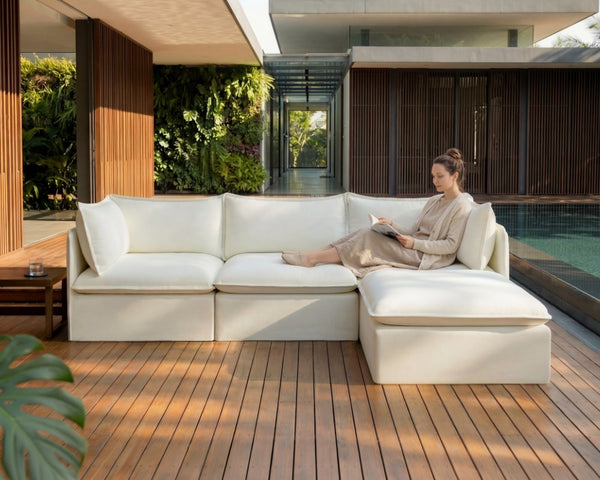 Lifestyle image of a woman lounging across Chicory’s Modular Outdoor Washable 3-Seater Sectional in Classic Canvas Cloud fabric, highlighting the outdoor sister brand Chicory.