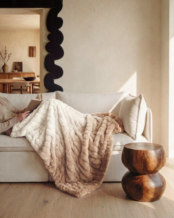 Lifestyle image of a living room sofa and person lounging with a throw blanket highlighting the washable cloud throw blanket.