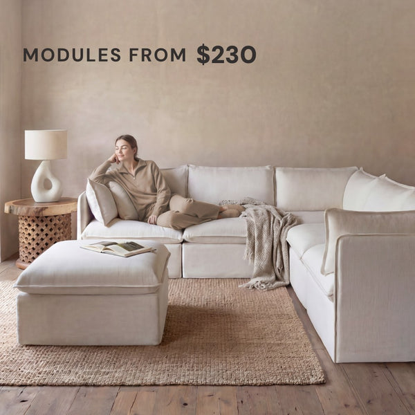Lifestyle image of a modular 5-seater sofa corner sectional with ottoman in white fabric with woman lounging comfortably