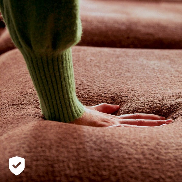 Close up of seat cushion that a women is pushing down on of a modular sofa in chestnut red fabric, showing the comfort and durability of the commercial grade fabric.