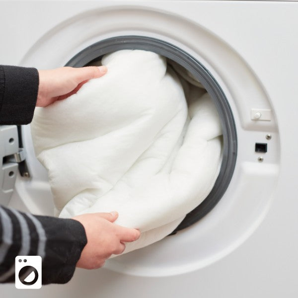 Close up of a duvet cover being put into a washing machine, highlighting the washable duvet-style cover system.