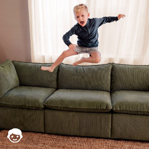 Lifestyle image of a child jumping off a modular 3-seater sofa in Olivine fabric, highlighting durable construction for active family homes.